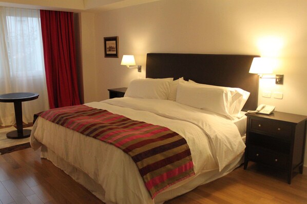 Une chambre d’hôtel avec un lit, deux tables de chevet, une lampe, un téléphone et un rideau rouge.