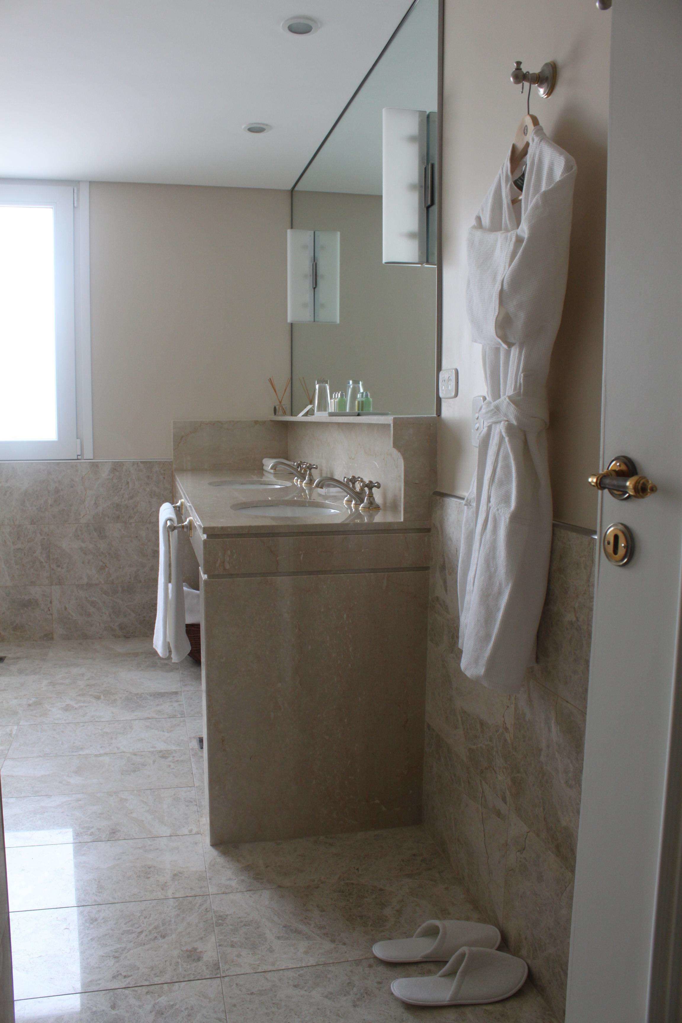 A bathroom with a marble sink, a robe hanging on the wall, and a pair of slippers on the floor.