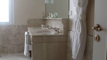 A bathroom with a marble sink, a robe hanging on the wall, and a pair of slippers on the floor.