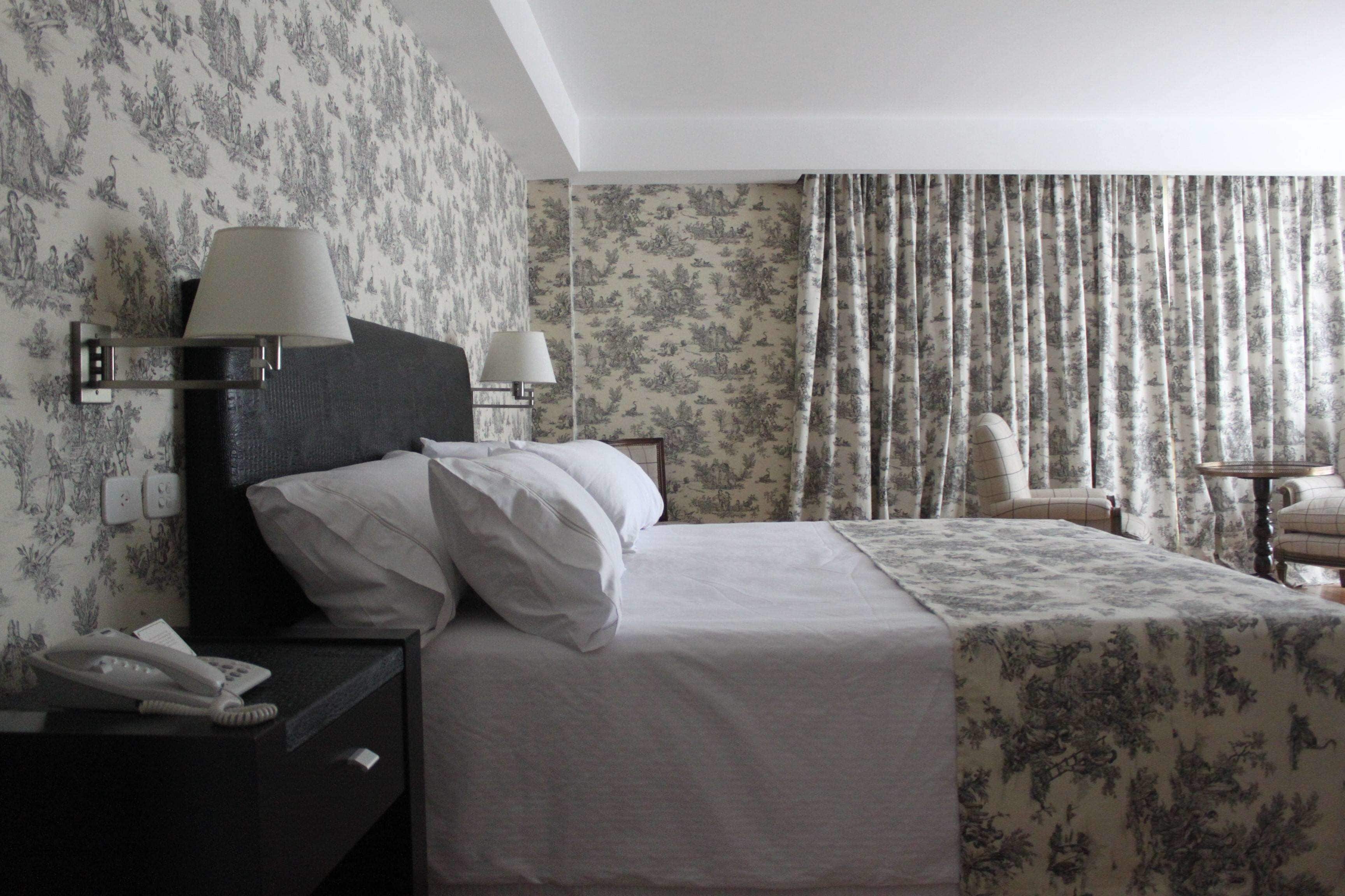 A hotel room with a bed, two bedside lamps, a telephone, a chair, and a table.