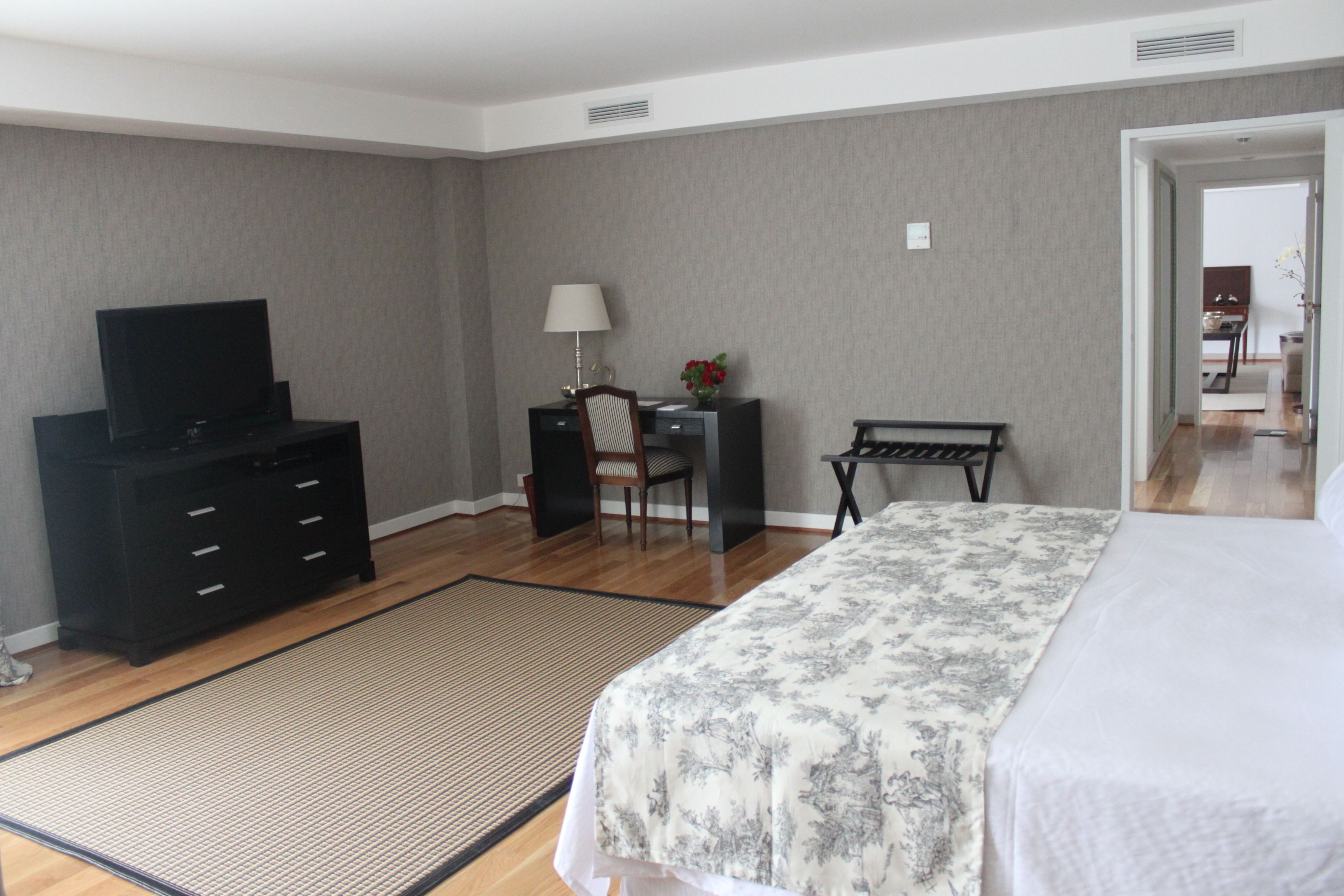 A hotel room with a bed, a desk, a chair, a television, and a desk lamp.