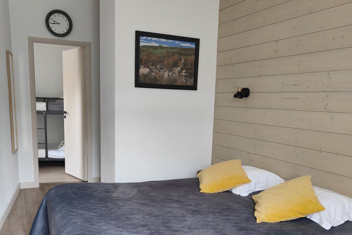 A bedroom with a bed, a wooden wall panel, a framed picture, and a clock on the wall.