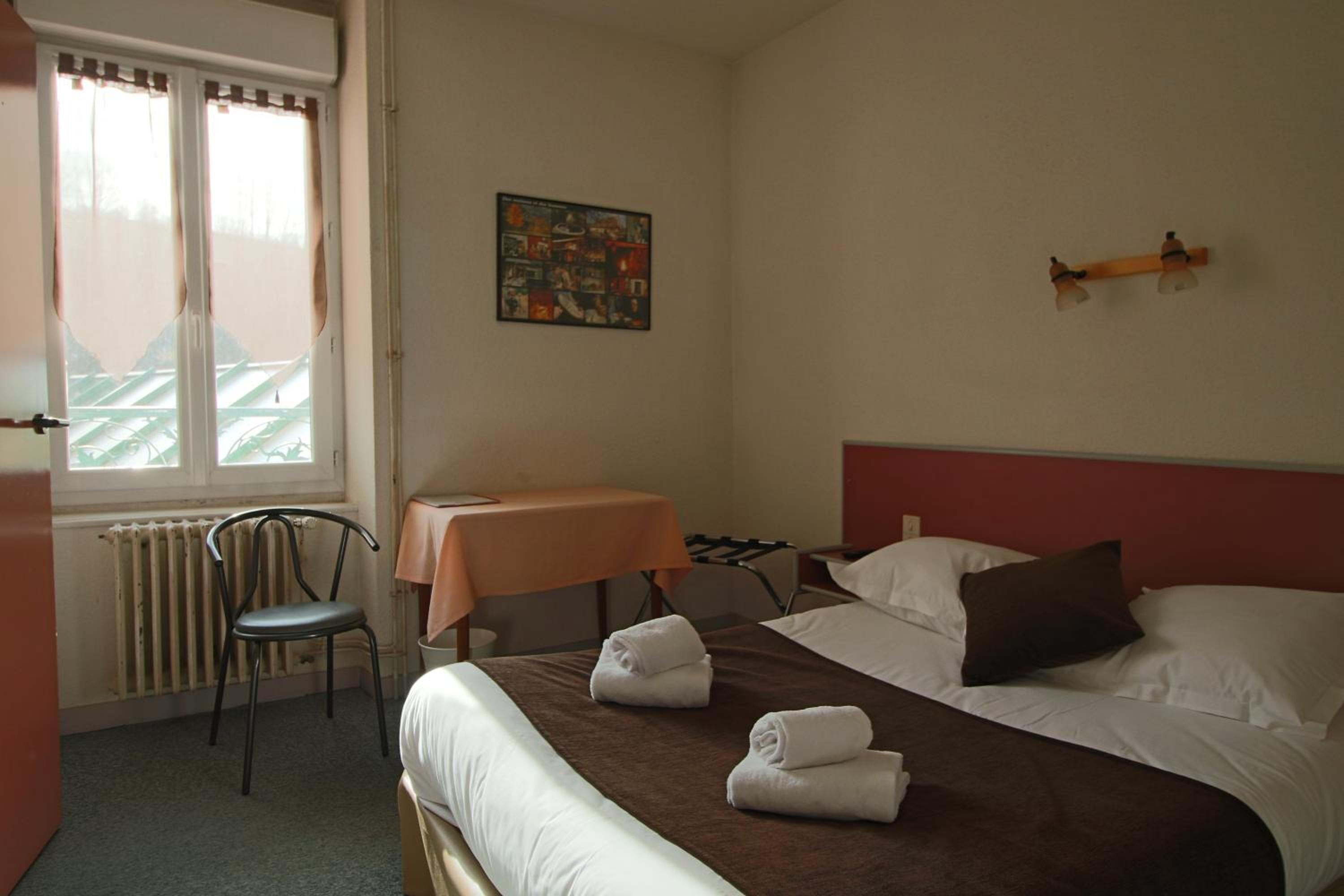 A hotel room with a bed, a chair, a table, and a radiator.