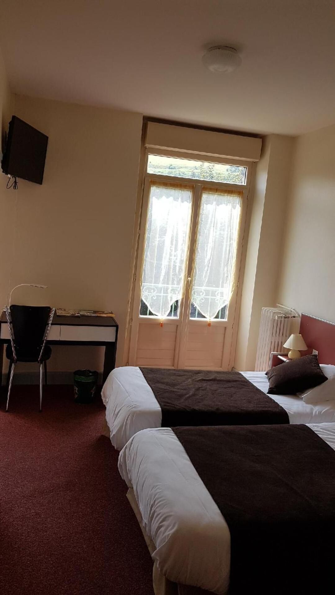 A hotel room with two beds, a desk with a chair, a radiator, and a TV on the wall.