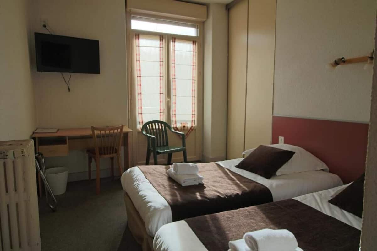 A hotel room with two beds, a desk, a chair, and a TV mounted on the wall.