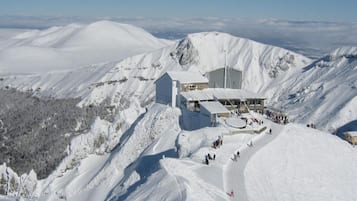 A snow-covered mountain with a lodge featuring a large building and a smaller structure, surrounded by snow-covered slopes and a clear sky.