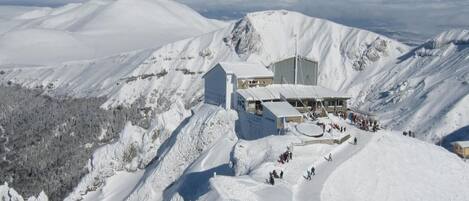A snow-covered mountain with a lodge featuring a large building and a smaller structure, surrounded by snow-covered slopes and a clear sky.