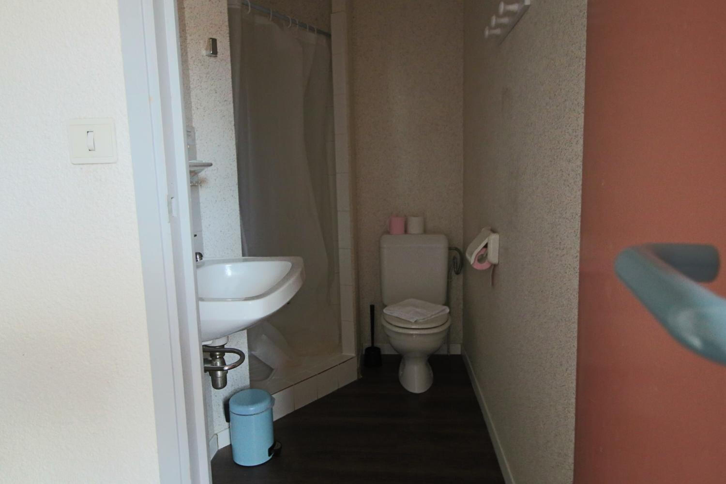 Un baño estrecho con un lavabo blanco, un inodoro y un cubo de basura azul.