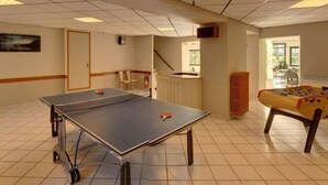 Een kamer met een tafeltennistafel, een tafelvoetbaltafel en een kleine kitchenette.