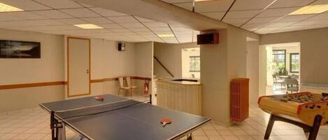 Une pièce équipée d’une table de ping-pong, d’un baby-foot et d’un petit coin cuisine.