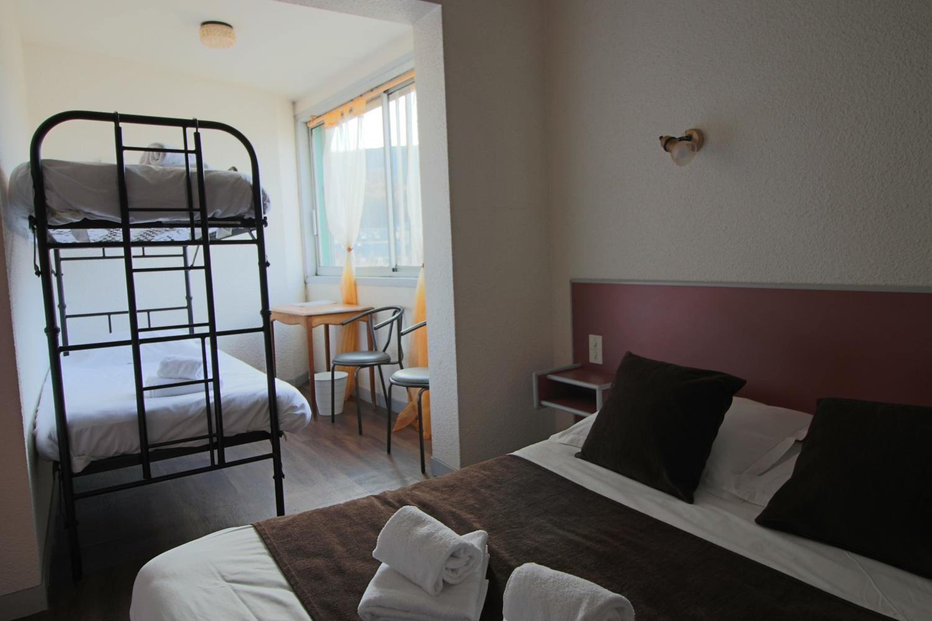 A room with a bunk bed, a single bed, a desk with a chair, and a small table.