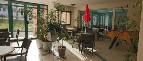 An indoor dining area with tables and chairs, potted plants, and a red umbrella.