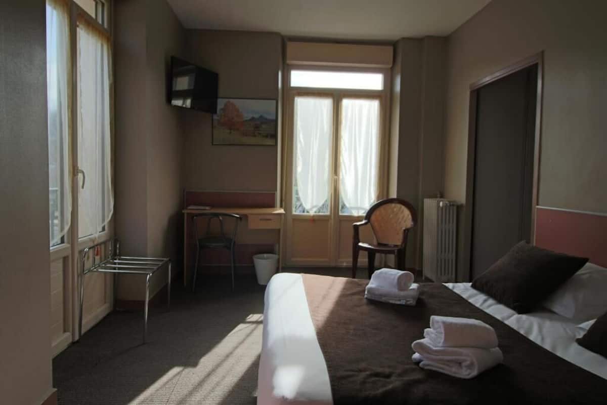 A hotel room with a bed, a desk, a chair, and a window with curtains.