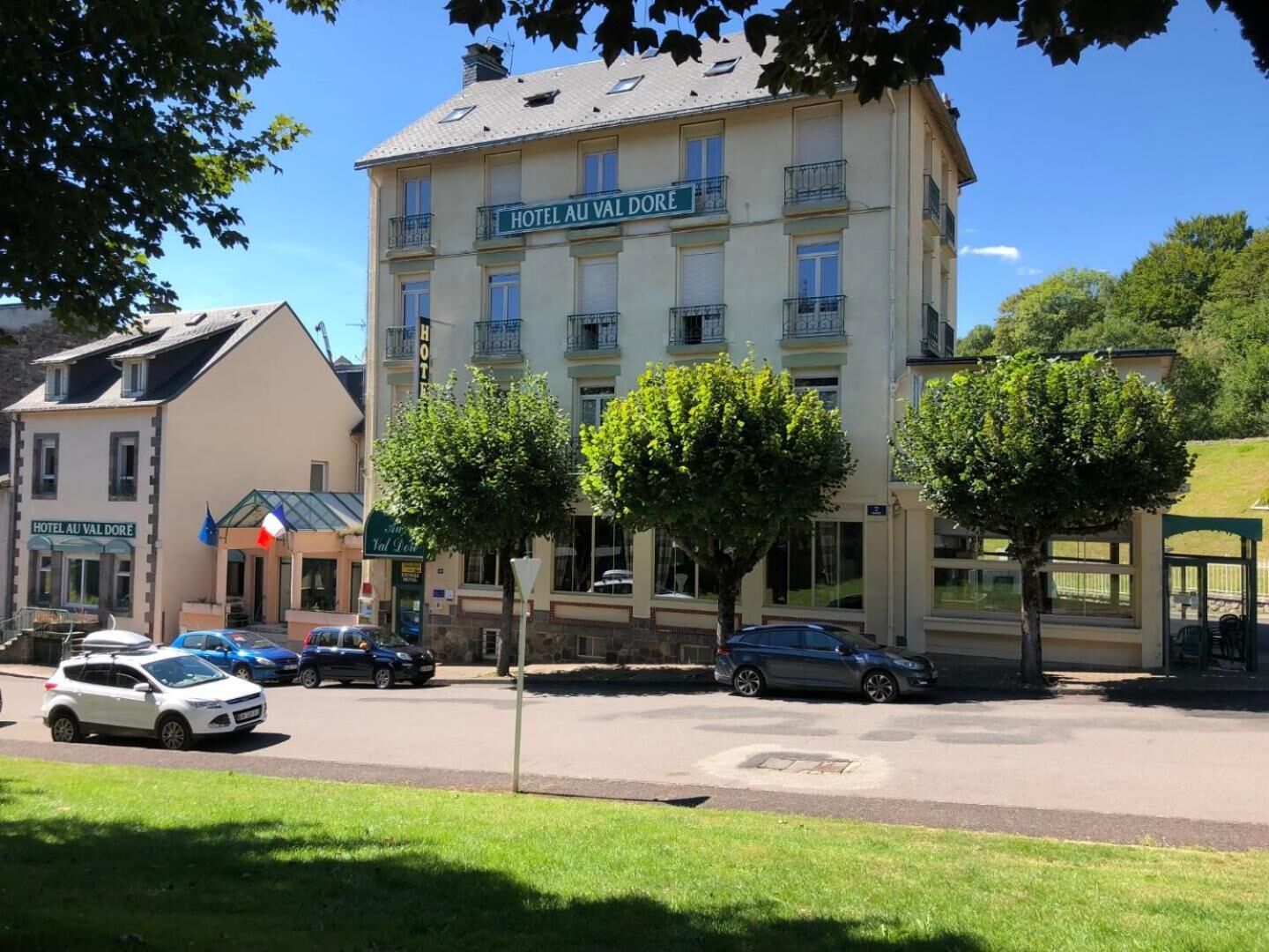A hotel building with balconies, a parking area, and trees in front.