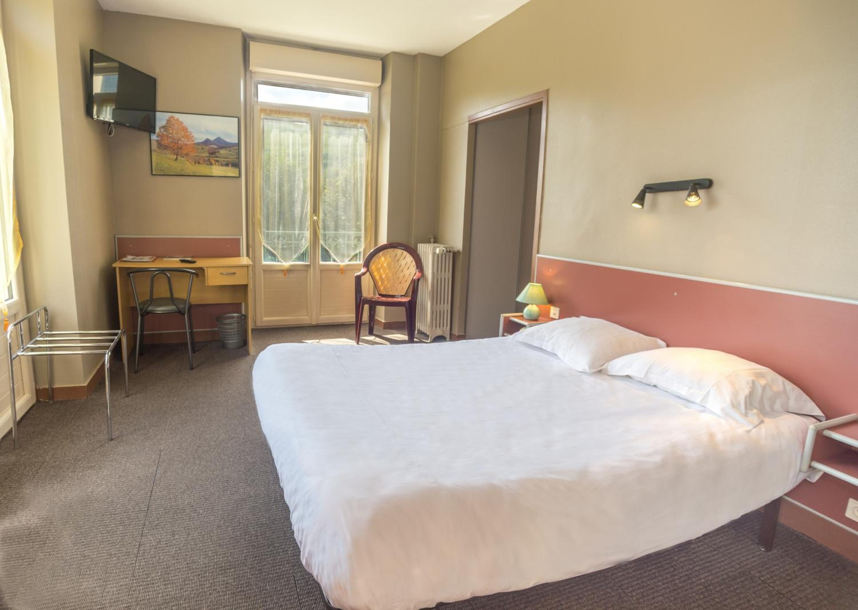 A hotel room with a large bed, a desk, a chair, a radiator, and a television mounted on the wall.