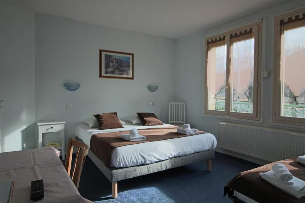A hotel room with a large bed, a smaller bed, a desk, and a chair. There are towels on the beds and a remote control on the desk.