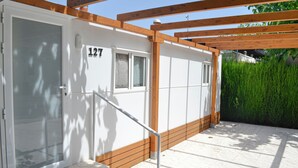 A white building with the number 127, a wooden pergola, and a tiled patio area. - Camping Arena Blanca (Benidorm)