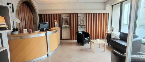 Un espace d’accueil comprenant un bureau incurvé, un fauteuil en cuir noir, une petite table et un canapé.