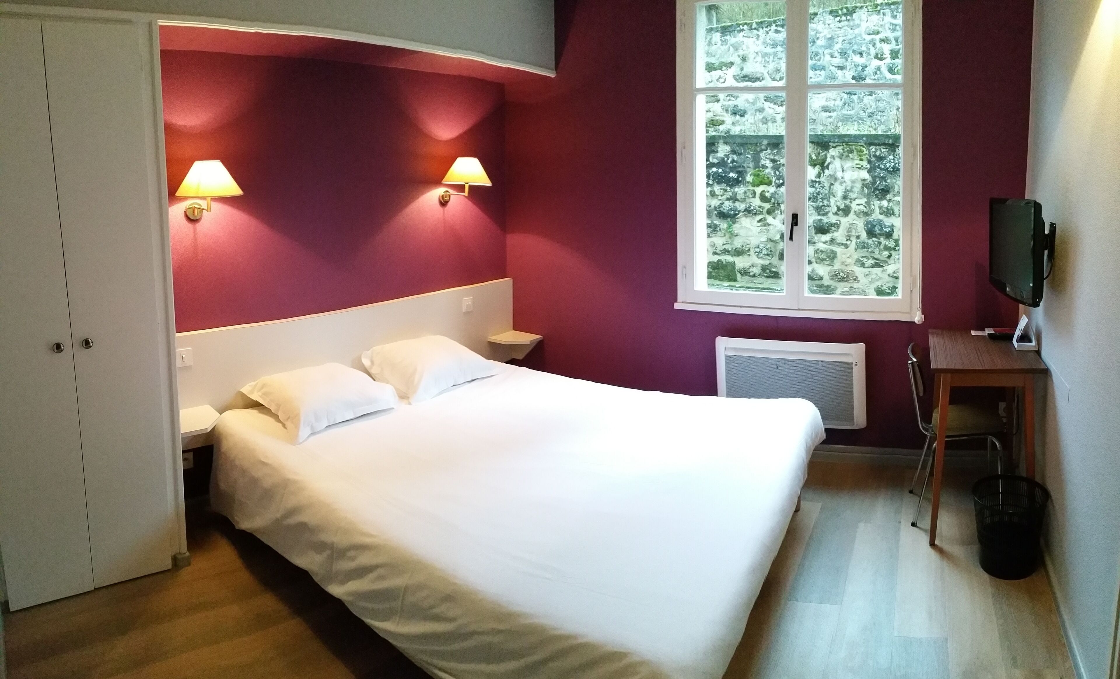 Une chambre à coucher avec un lit, deux lampes de chevet, une fenêtre donnant sur un beau paysage, un bureau et un radiateur.