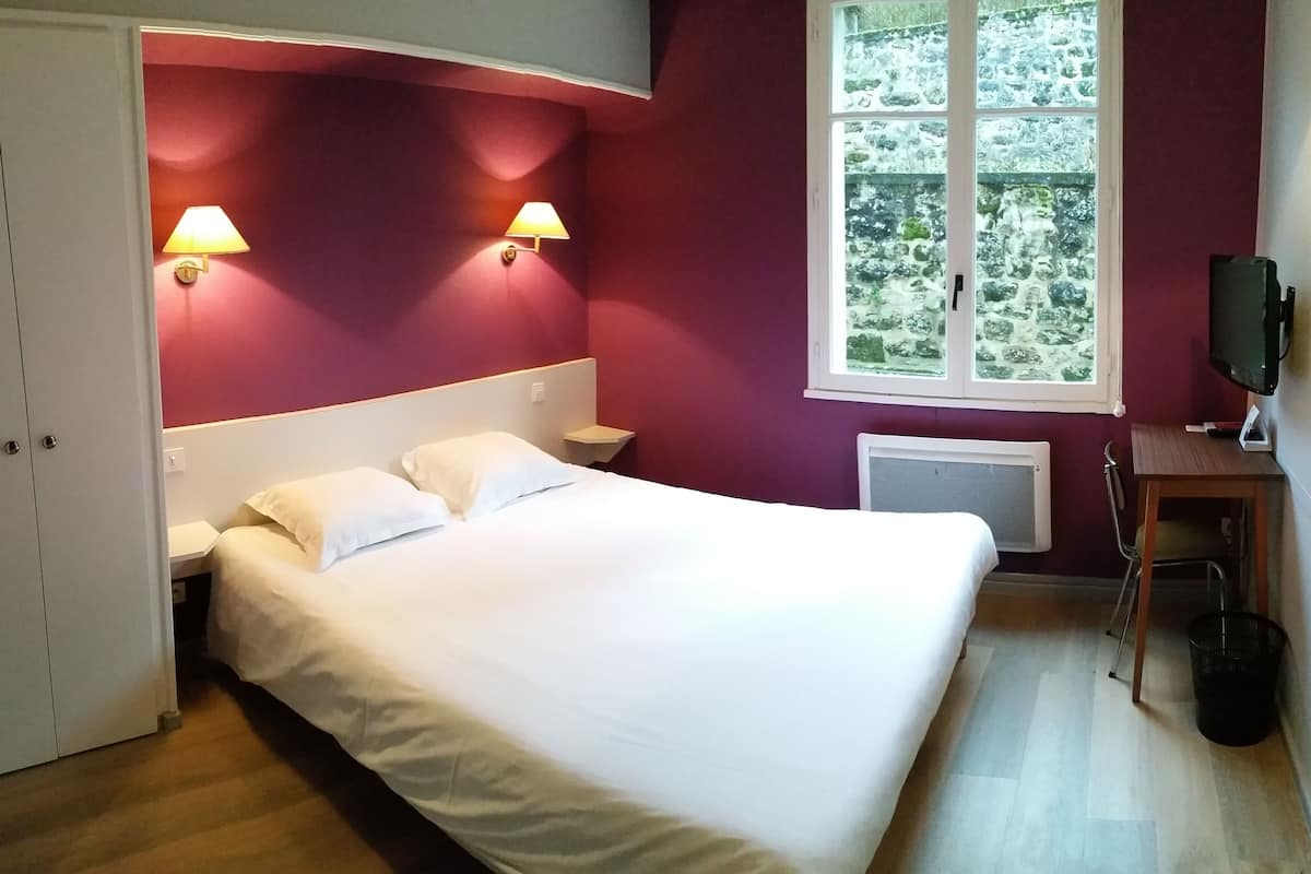 A bedroom with a bed, two bedside lamps, a window with a view, a desk, and a radiator.