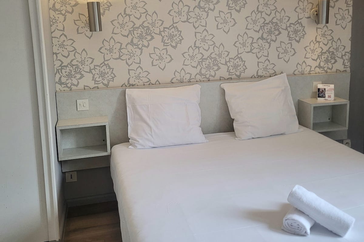 A hotel room with a large bed, two nightstands, and floral wallpaper.