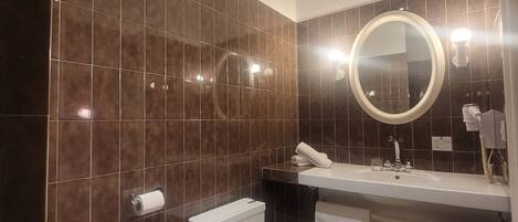Un baño moderno con baldosas marrón oscuro, un inodoro blanco, un lavamanos con espejo y toallas.