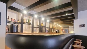Una zona de bar con una barra negra curva, estantes con botellas, vasos y un cartel en la pared.