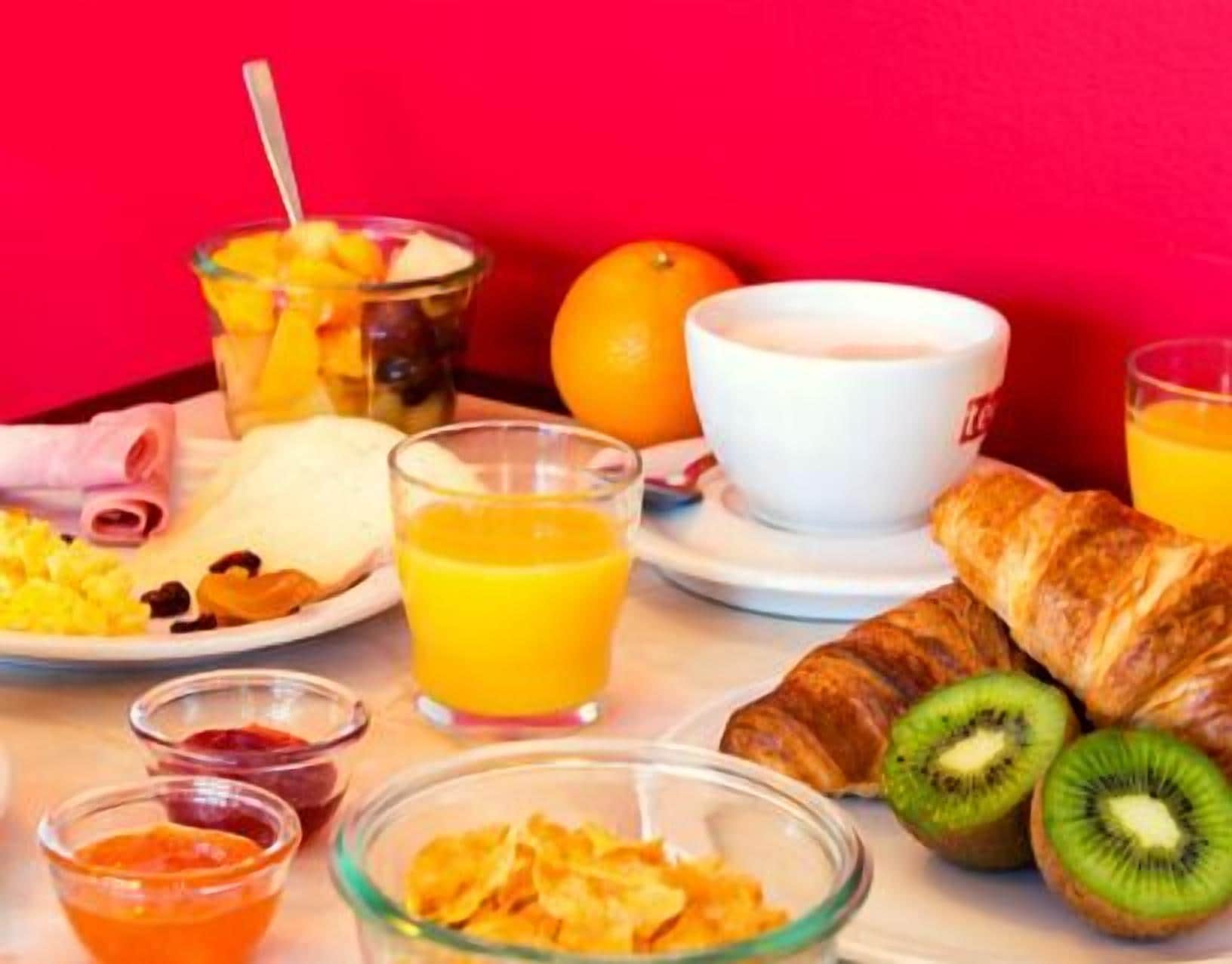 En frukostuppläggning med croissanter, skivor av kiwi, apelsinjuice och en skål med flingor.