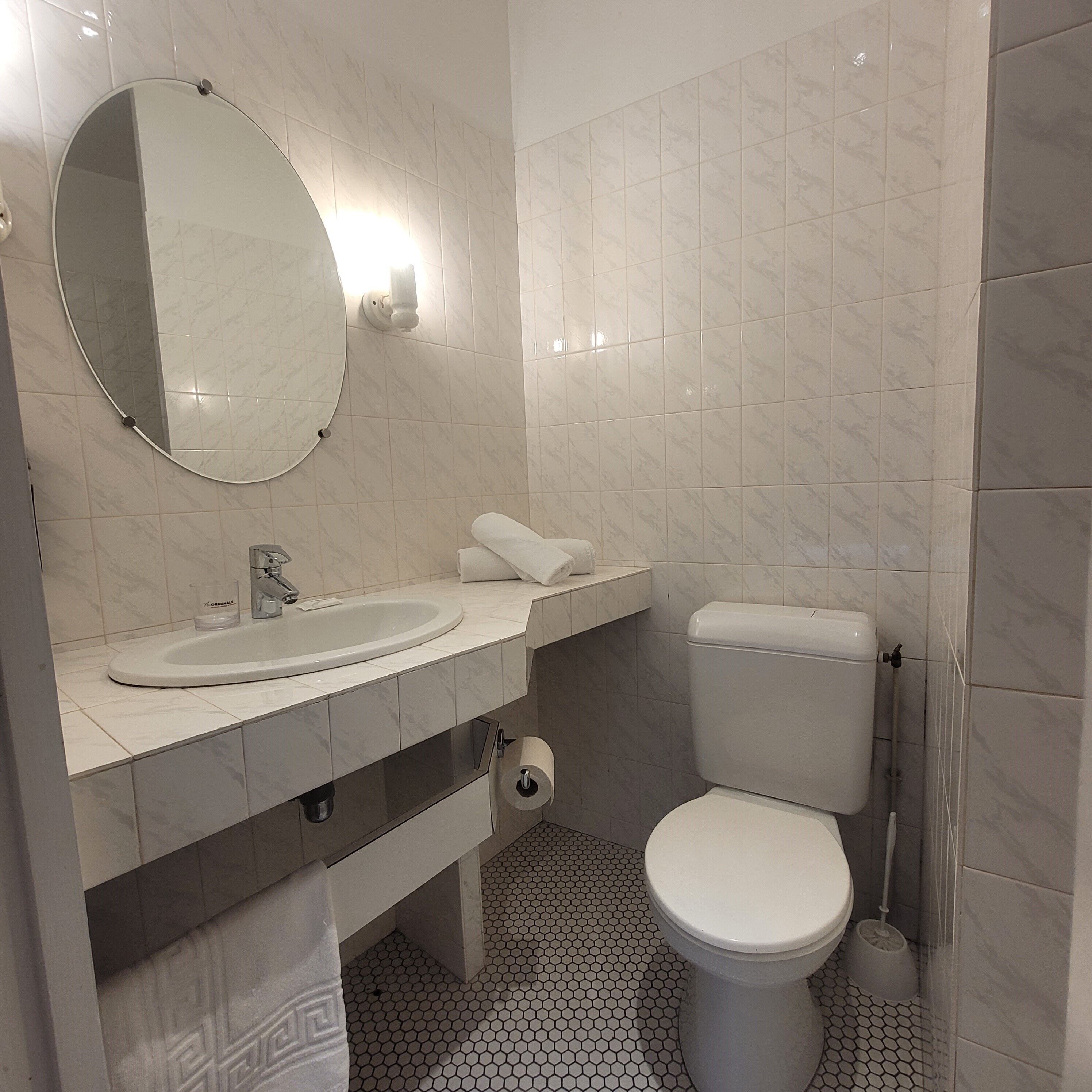 A bathroom with a round mirror, a sink, a toilet, and a toilet paper holder.