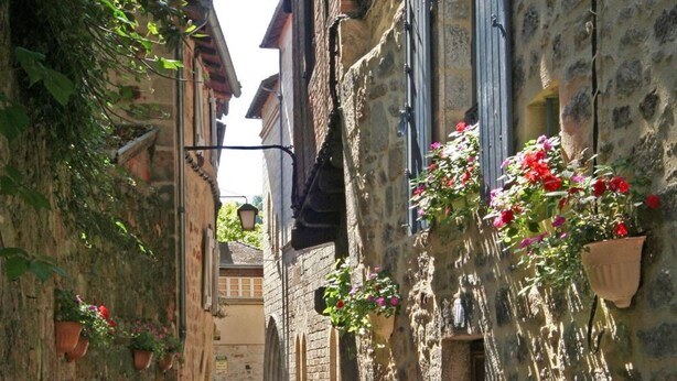 Un estrecho camino adoquinado flanqueado por edificios de piedra con macetas de flores en las paredes.