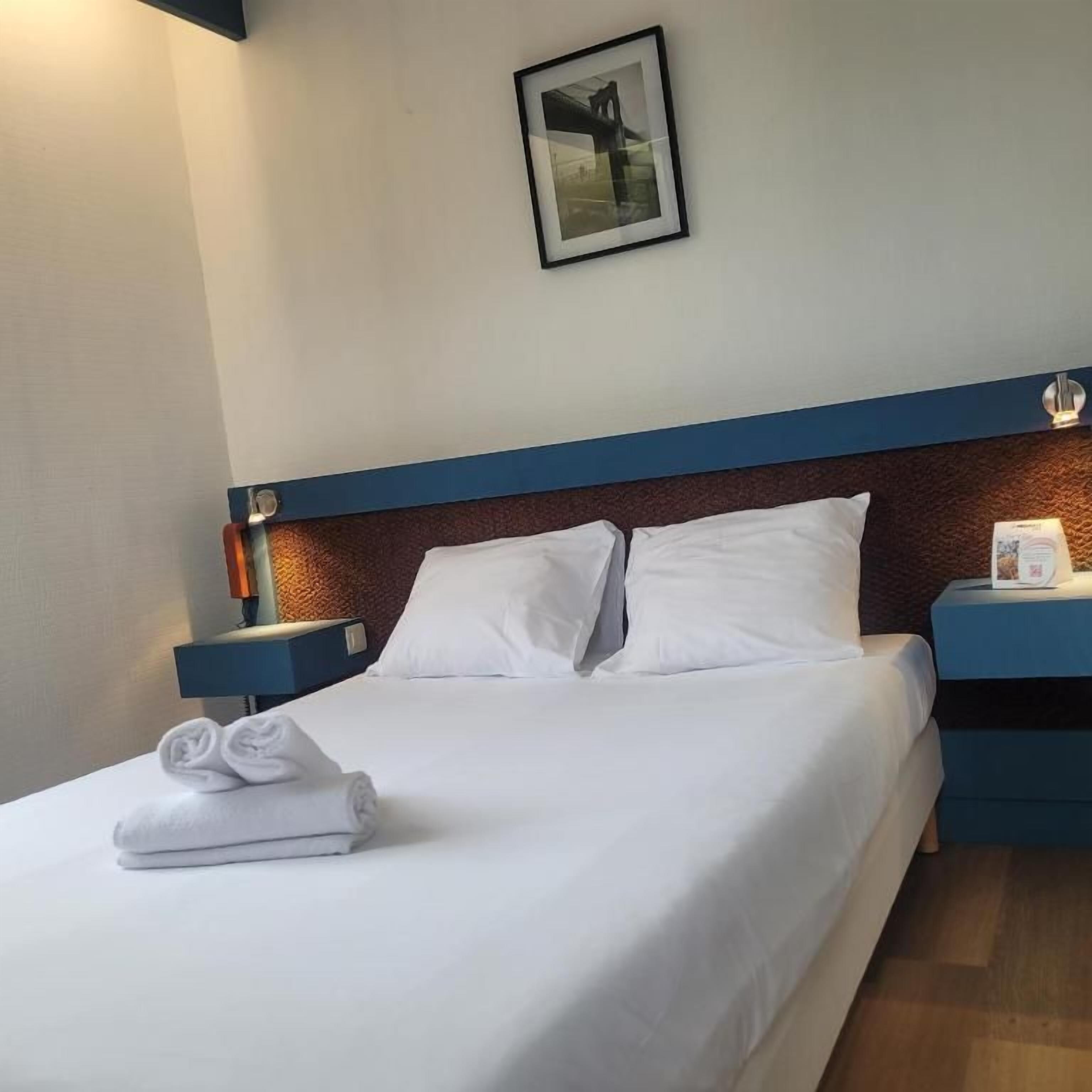 Una habitación de hotel con una cama bien hecha, un cuadro en la pared y una mesita de noche con una lámpara.
