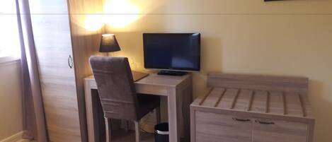 Una habitación pequeña y bien iluminada con escritorio, silla, televisor y cama.
