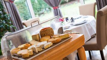 A cheese board with various types of cheese and bread on a wooden table in a room with a view of greenery outside.