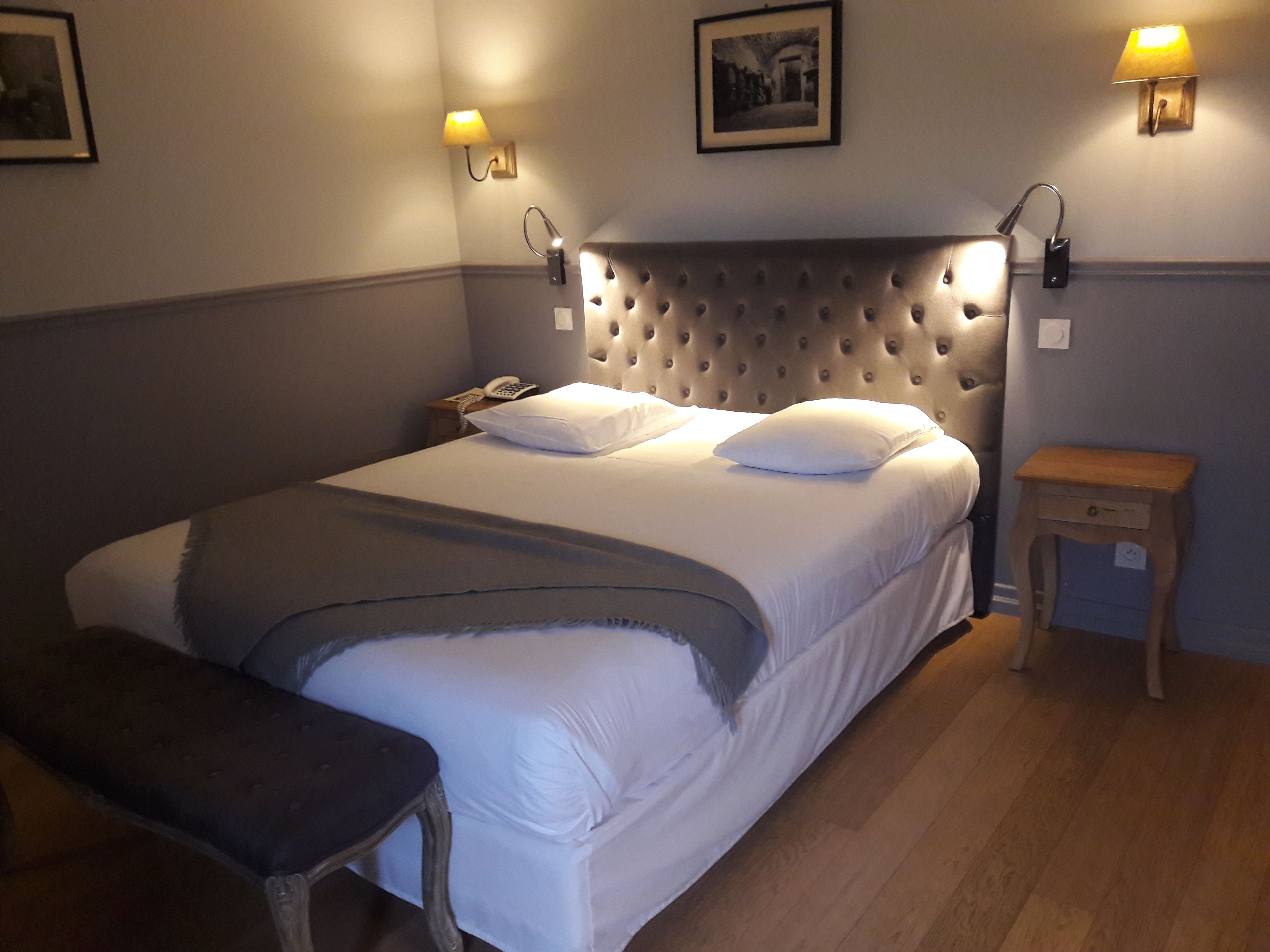 A neatly made bed with a tufted headboard, two bedside lamps, and a small wooden nightstand.