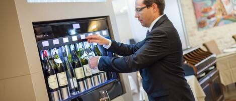 A man selecting a wine bottle from a wine cooler in a well-lit room with a modern interior design.