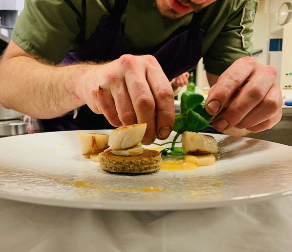 A person preparing a dish with a slice of bread, a leaf, and a piece of meat on a plate.
