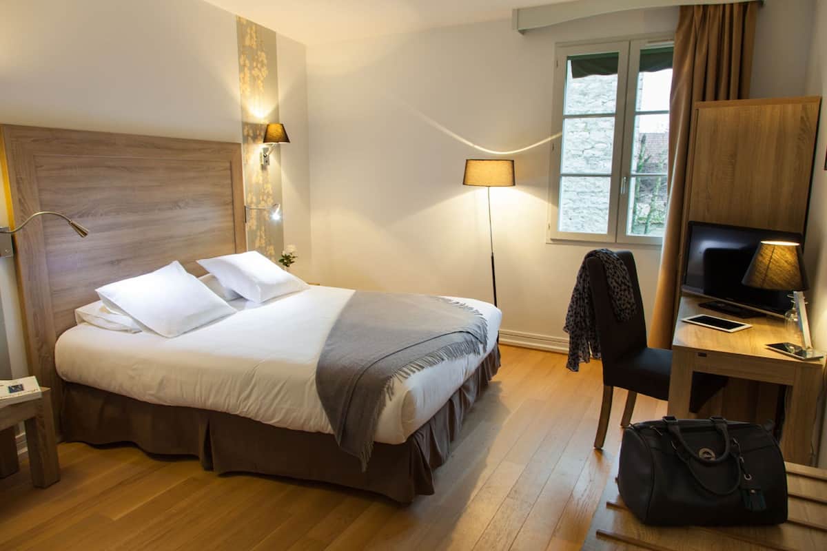 Habitación de hotel con cama, lámparas de noche, escritorio con computadora, una silla y ventana con cortinas.