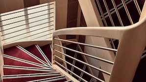 A modern staircase with a wooden handrail and metal balusters, leading to a landing with a red carpet. - Hôtel Saint Martin (Orléans)