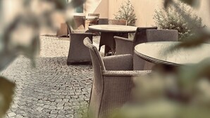 An outdoor patio area with wicker furniture and a stone floor. - Hôtel Saint Martin (Orléans)