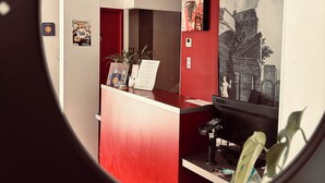 A reception area with a red counter, a computer, and a wall-mounted artwork. - Hôtel Saint Martin (Orléans)