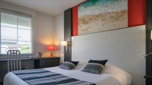 Una habitación de hotel con una cama grande, un escritorio con lámpara, una silla y un cuadro con una playa.