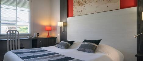 A hotel room with a large bed, a desk with a lamp, a chair, and a painting of a beach scene.