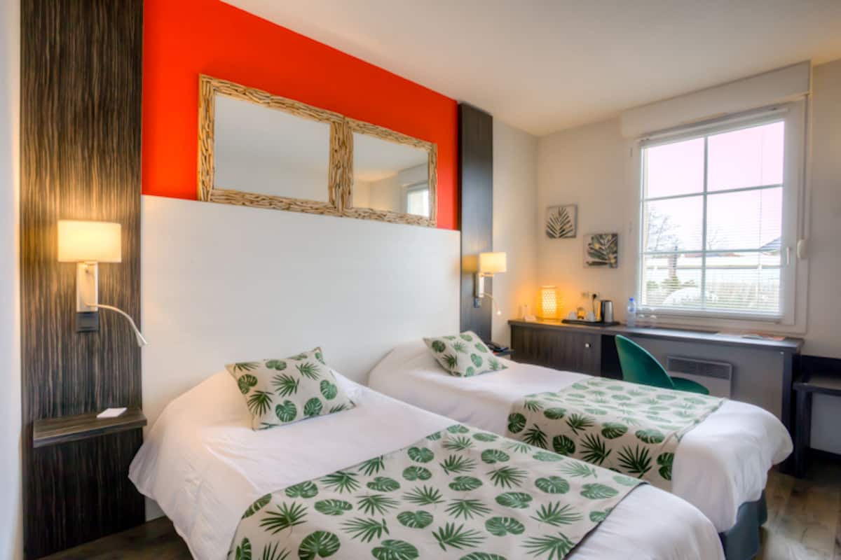 A hotel room with two beds, a desk, a chair, a large window, and a mirror on the wall.