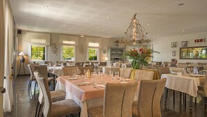 Un comedor espacioso con varias mesas dispuestas para comer, un candelabro y ventanas amplias que dejan entrar luz natural.