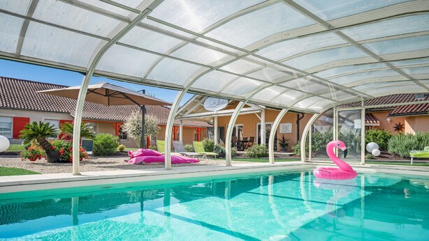 Un área de piscina con una estructura de cristal, sillas de descanso y un flotador con forma de flamenco.