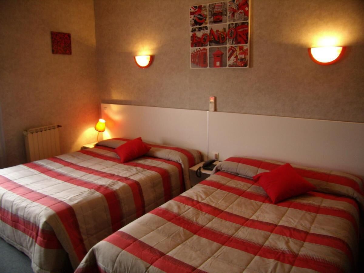 A room with two beds, each with a red and beige checkered bedspread, a small bedside table, and a wall-mounted light fixture.