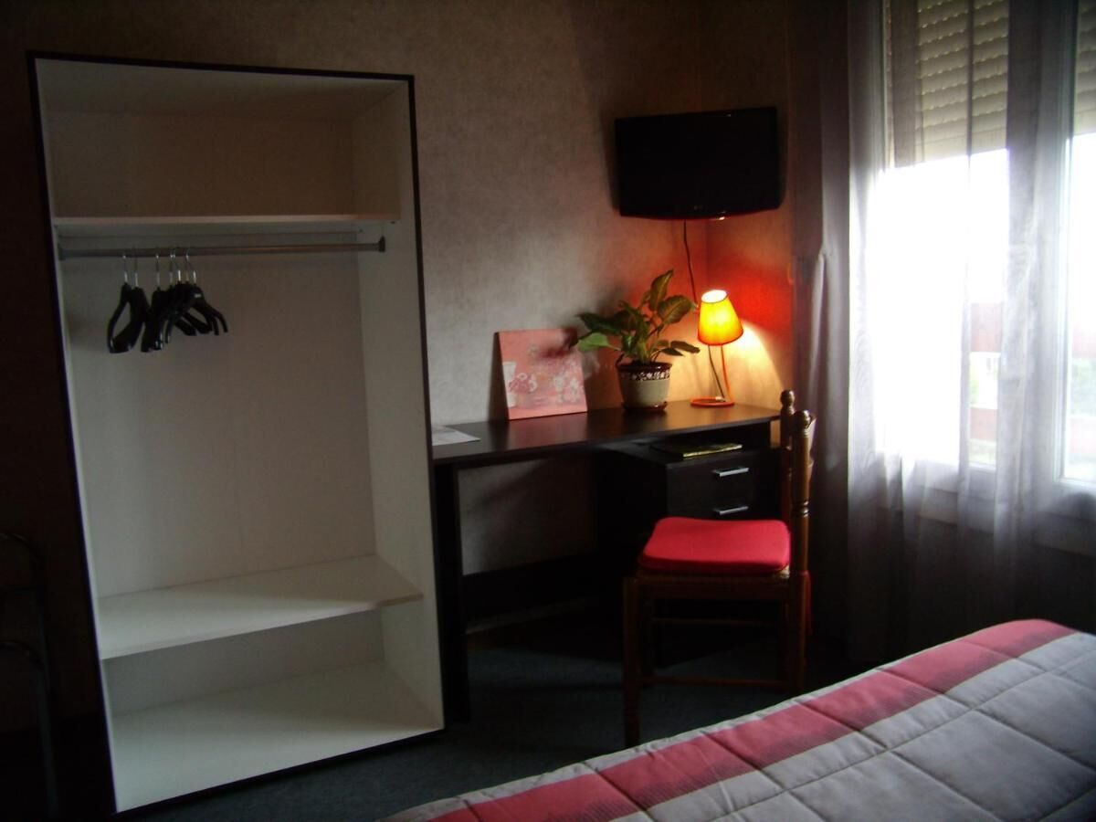 A hotel room with a bed, a desk with a chair, a television, and a wardrobe.