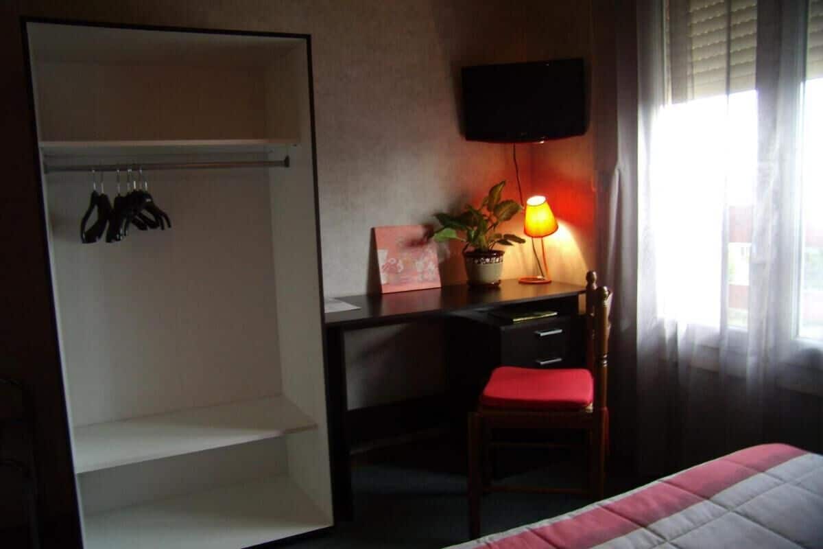 A hotel room with a bed, a desk with a chair, a television, and a wardrobe.
