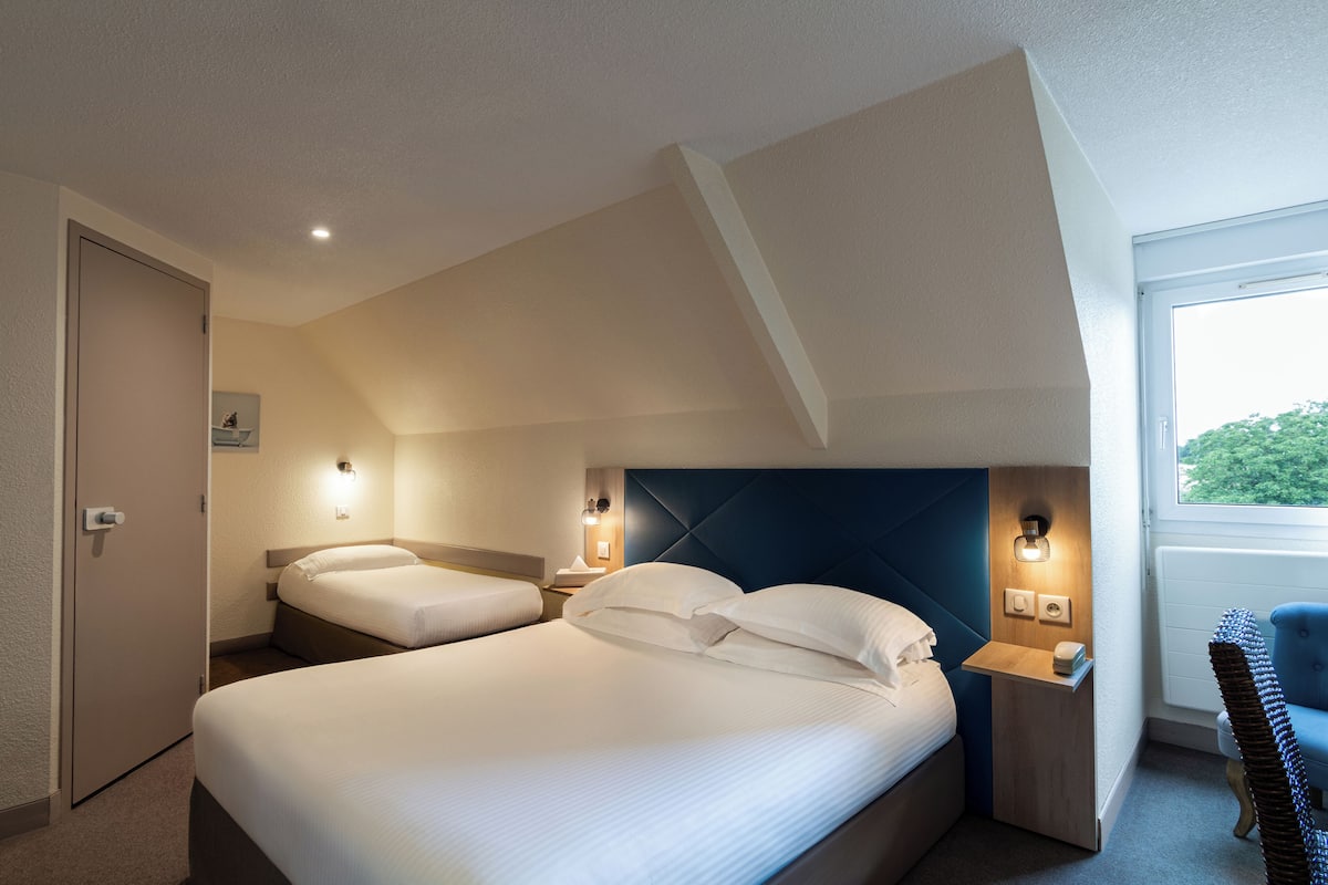A hotel room with two beds, a window with a view, and a small table with a chair.