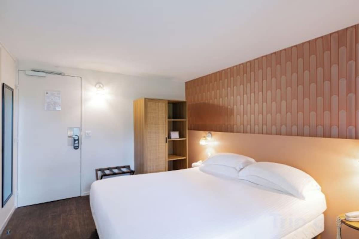 A hotel room with a bed, a wardrobe, a desk, and a door.